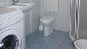 Een kleine badkamer met een wasmachine, wastafel, toilet en douchecabine.