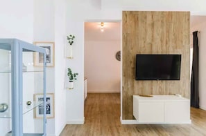 A modern living room with a wooden accent wall, a flat-screen TV, and a glass-fronted cabinet with framed photos. - Holiday apartment with wellness facilities and shared swimming pool (Novi Vinodolski)