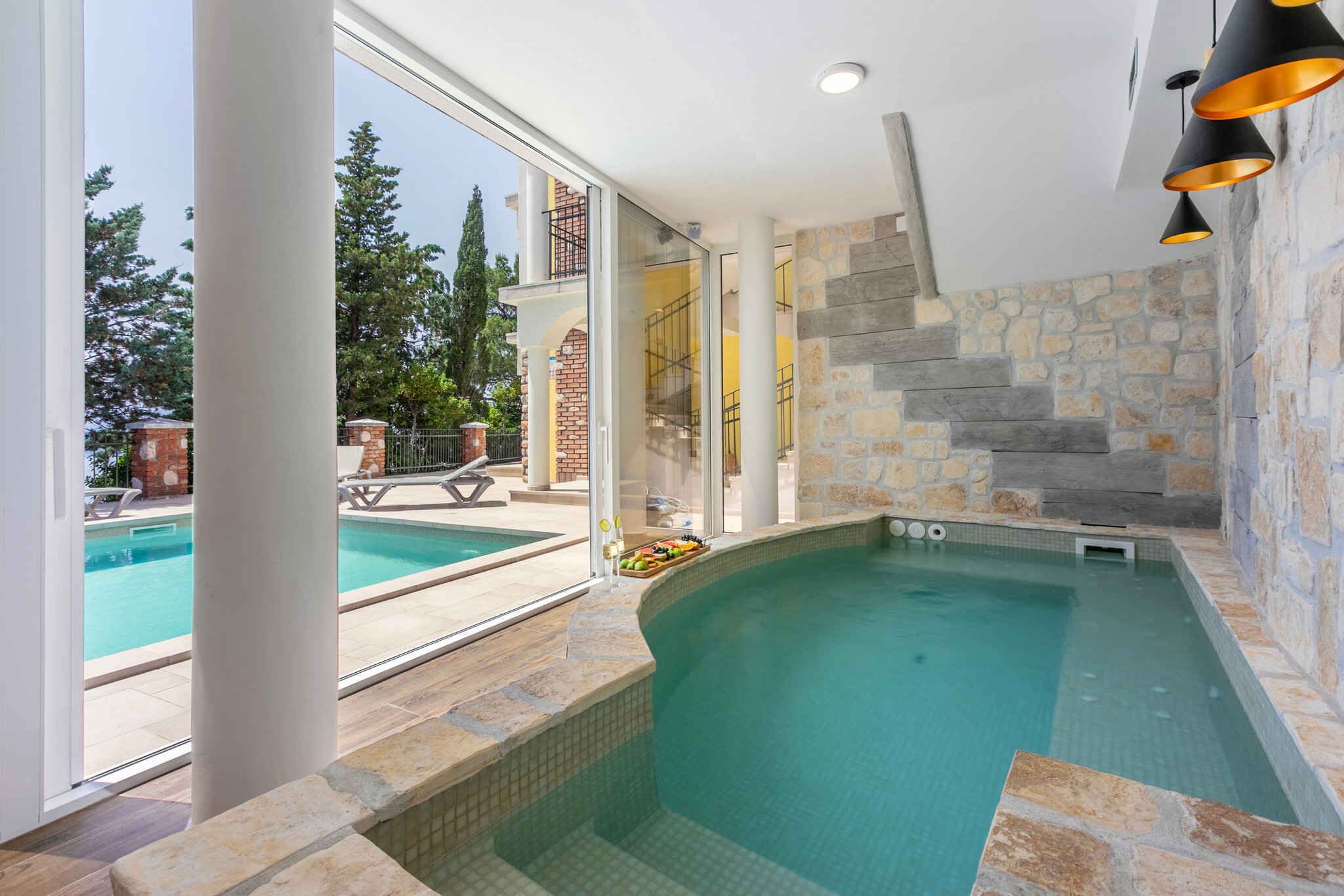 A modern indoor swimming pool with stone walls and a glass door leading outside.