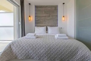 Une chambre moderne avec un grand lit, deux lampes de chevet et une vue dégagée sur l’extérieur grâce à une grande fenêtre.