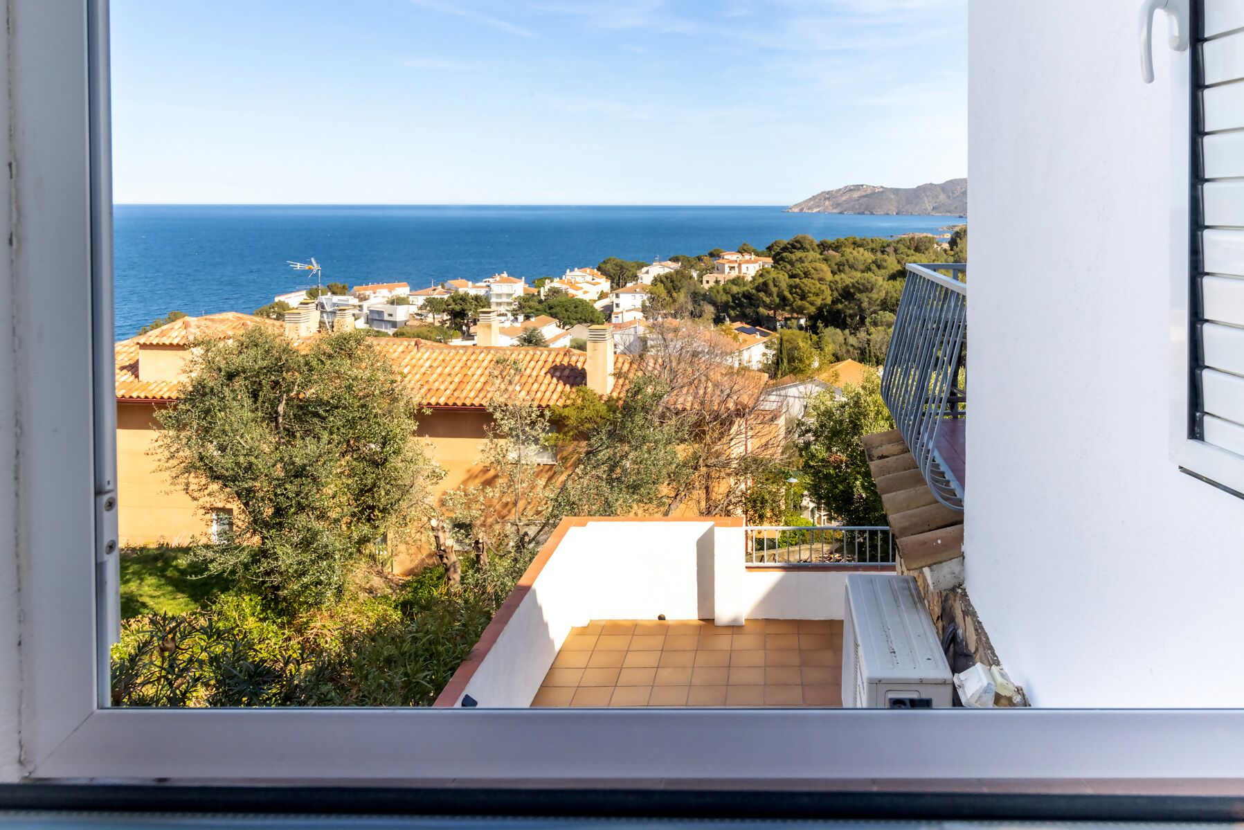 A view from a window overlooking a coastal town with buildings, trees, and the sea.