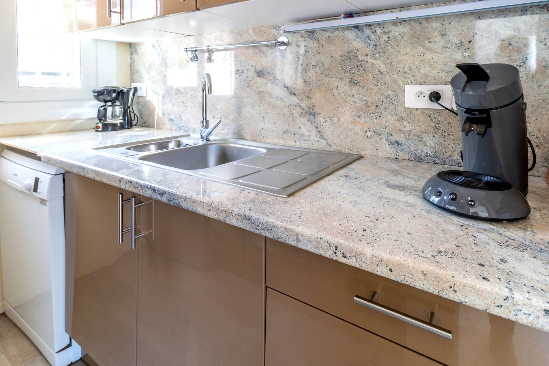 A kitchen with a granite countertop, stainless steel sink, and a coffee maker.