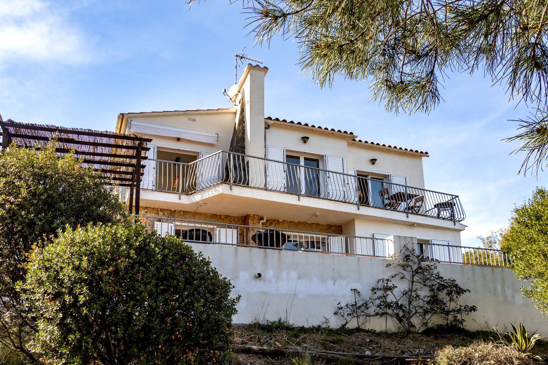 A two-story building with balconies, a stone base, and surrounding greenery.