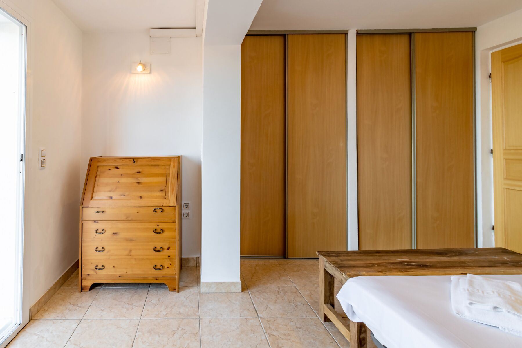 A bedroom with a wooden dresser, a bed, and a sliding wooden door closet.