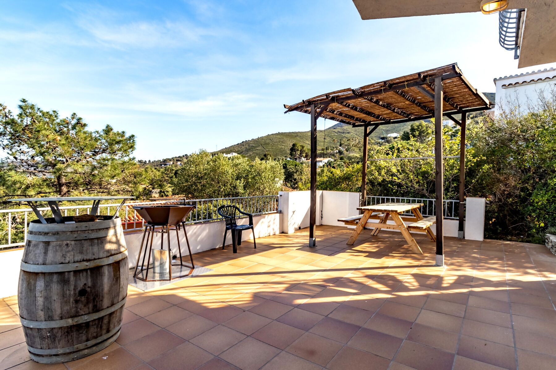 Eine Terrasse im Freien mit einer Holz-Pergola, einem Grill und einem Holzfass.