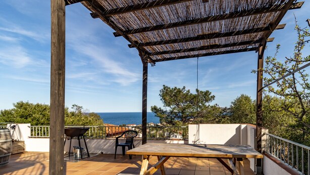 A wooden pergola with a view of the sea, a picnic table, and a grill on a tiled patio. - Fener de Dalt 86.2 - Apartment with views (Llança)