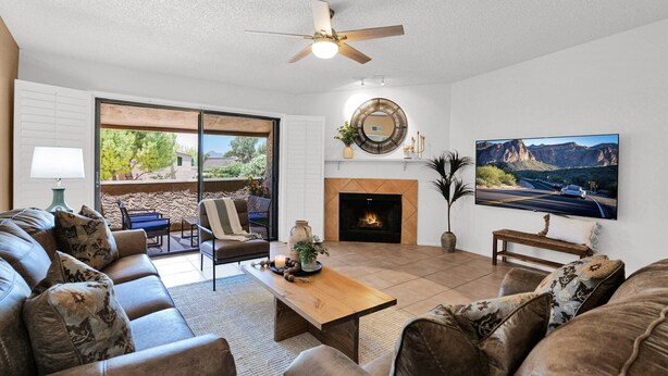 A living room with a fireplace, a ceiling fan, a TV, and a large window overlooking a patio. - The Western Bungalow - old town - bike path - pool (Scottsdale)
