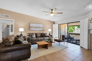A living room with a brown leather sofa, a wooden coffee table, and a ceiling fan. There is a sliding glass door leading to an outdoor patio. - The Western Bungalow - old town - bike path - pool (Scottsdale)