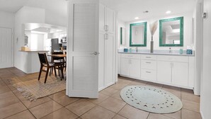 A modern kitchen with white cabinets, a dining area with a table and chairs, and a bathroom with a sink and mirrors. - The Western Bungalow - old town - bike path - pool (Scottsdale)