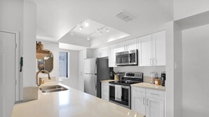 A modern kitchen with white cabinetry, stainless steel appliances, and a large island with a sink. - The Western Bungalow - old town - bike path - pool (Scottsdale)
