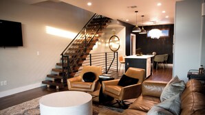 A modern living room with a staircase, leather furniture, and a round ottoman. - Private Rooftop Skyline Views - Walk To Pearl (San Antonio)