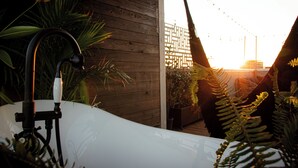 A white bathtub with a black faucet, surrounded by lush greenery and a wooden fence. - Private Rooftop Skyline Views - Walk To Pearl (San Antonio)