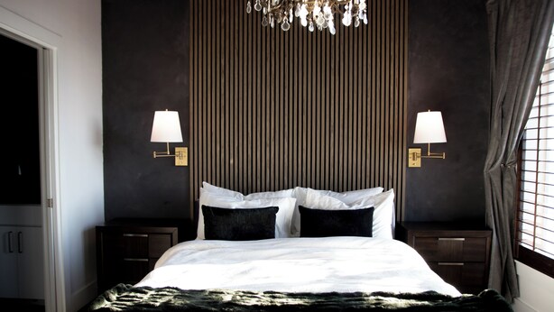 A bedroom with a large bed, two bedside tables, a chandelier, and a window with curtains. - Private Rooftop Skyline Views - Walk To Pearl (San Antonio)