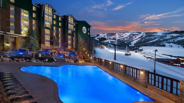 Un hotel con piscina, sillas de descanso y vistas a una montaña nevada.