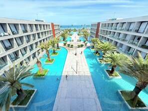 A hotel with a central pool, palm trees, and a view of the ocean. - Porto2Life Resort - Praia de Muro Alto (Ipojuca)