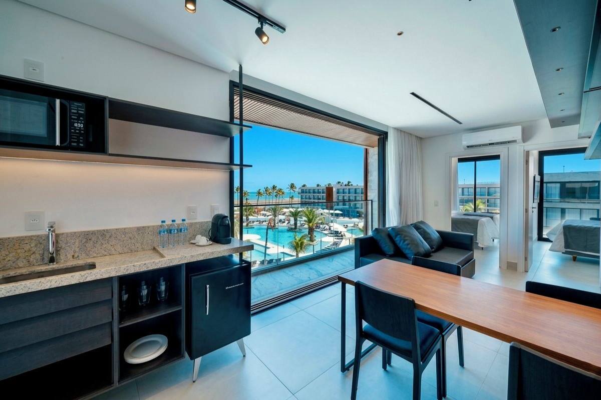 A modern kitchen with a built-in microwave, a sink, and a dining area with a view of a pool and beach.