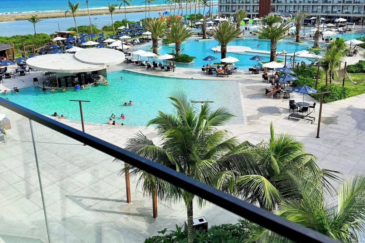 A resort with a large pool, palm trees, and a beach view.
