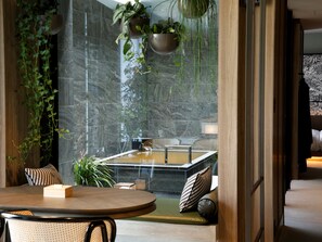 A modern interior with a round table, seating, a bathtub, and hanging plants. - Arima Hot Spring nebi (Kobe)