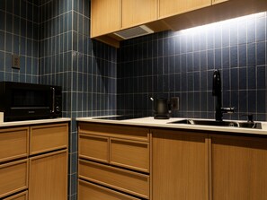 A kitchen with dark blue tiles, wooden cabinets, a black microwave, and a stainless steel sink. - Arima Hot Spring nebi (Kobe)