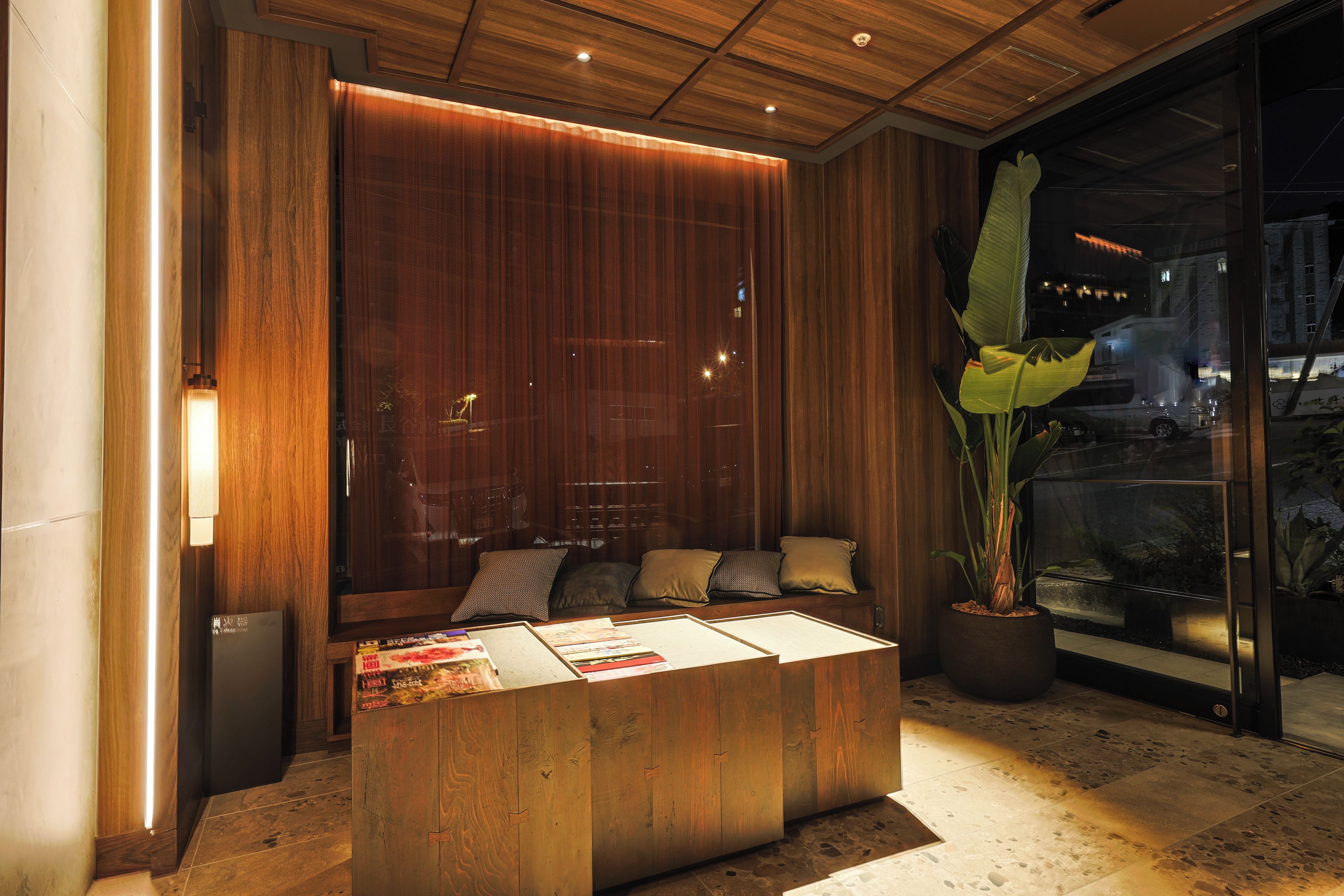 A modern interior with a wooden reception desk, seating area, and large windows.