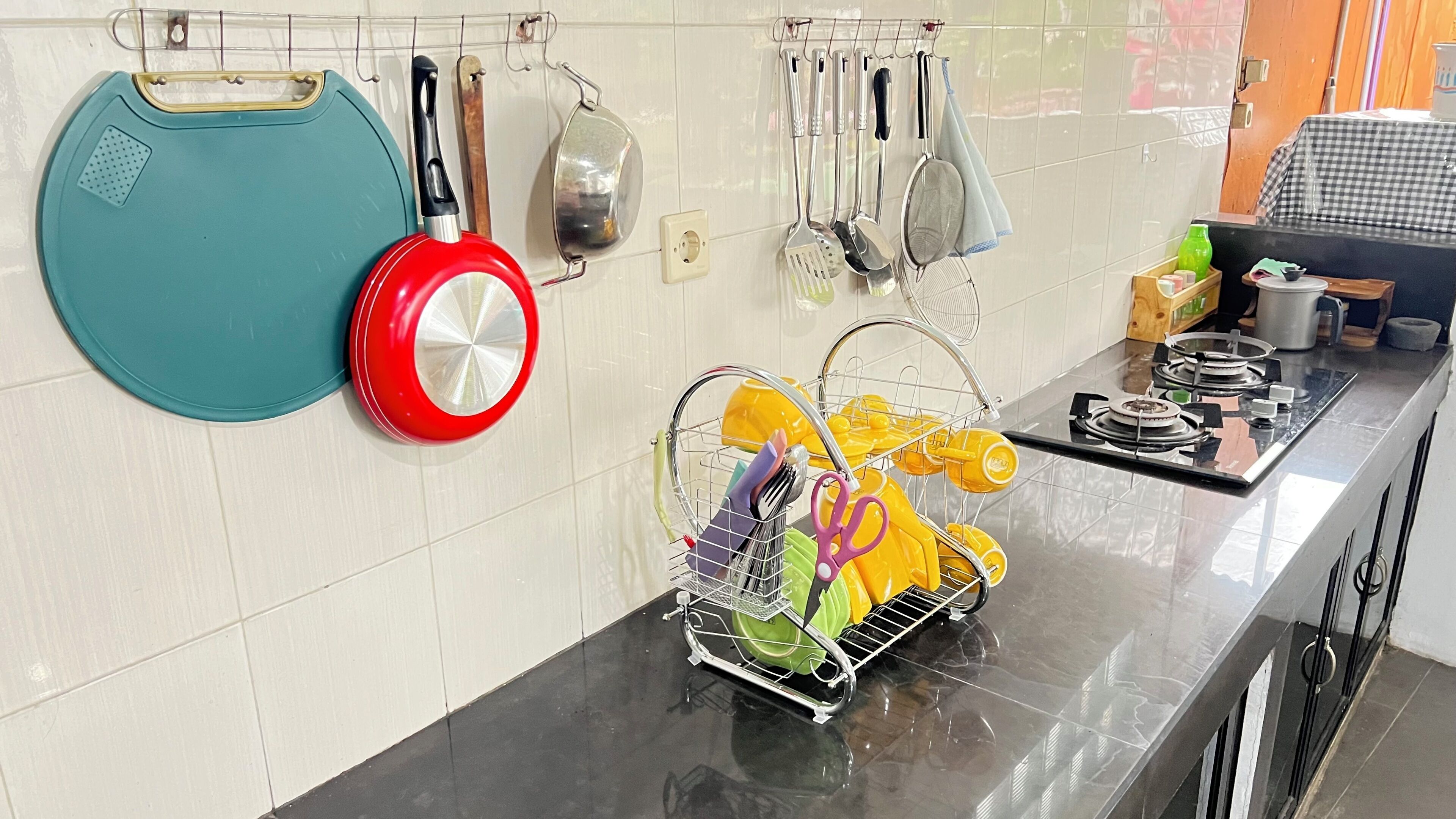 A kitchen with a dish rack holding utensils, a red pot, and a teal pan on the wall.