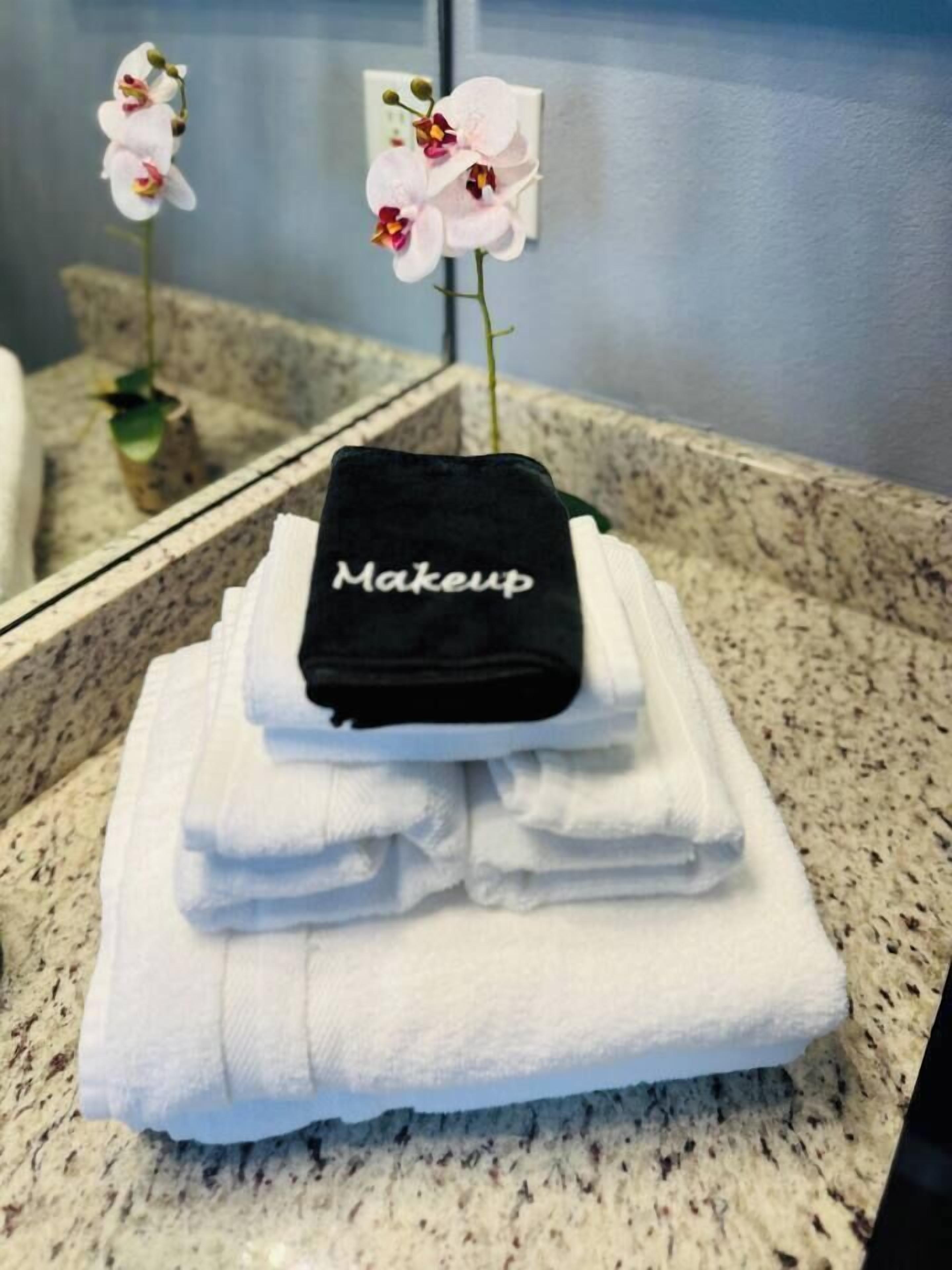 A bathroom with a granite countertop, a stack of white towels, and a black towel with 'Makeup' written on it.