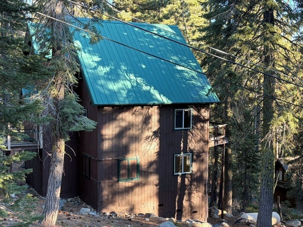 Une cabane rustique, dotée d’un toit métallique à pente, entourée d’une forêt dense.