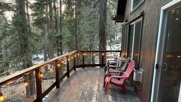 A wooden deck with string lights, a red chair, and a glass door leading to a building.
