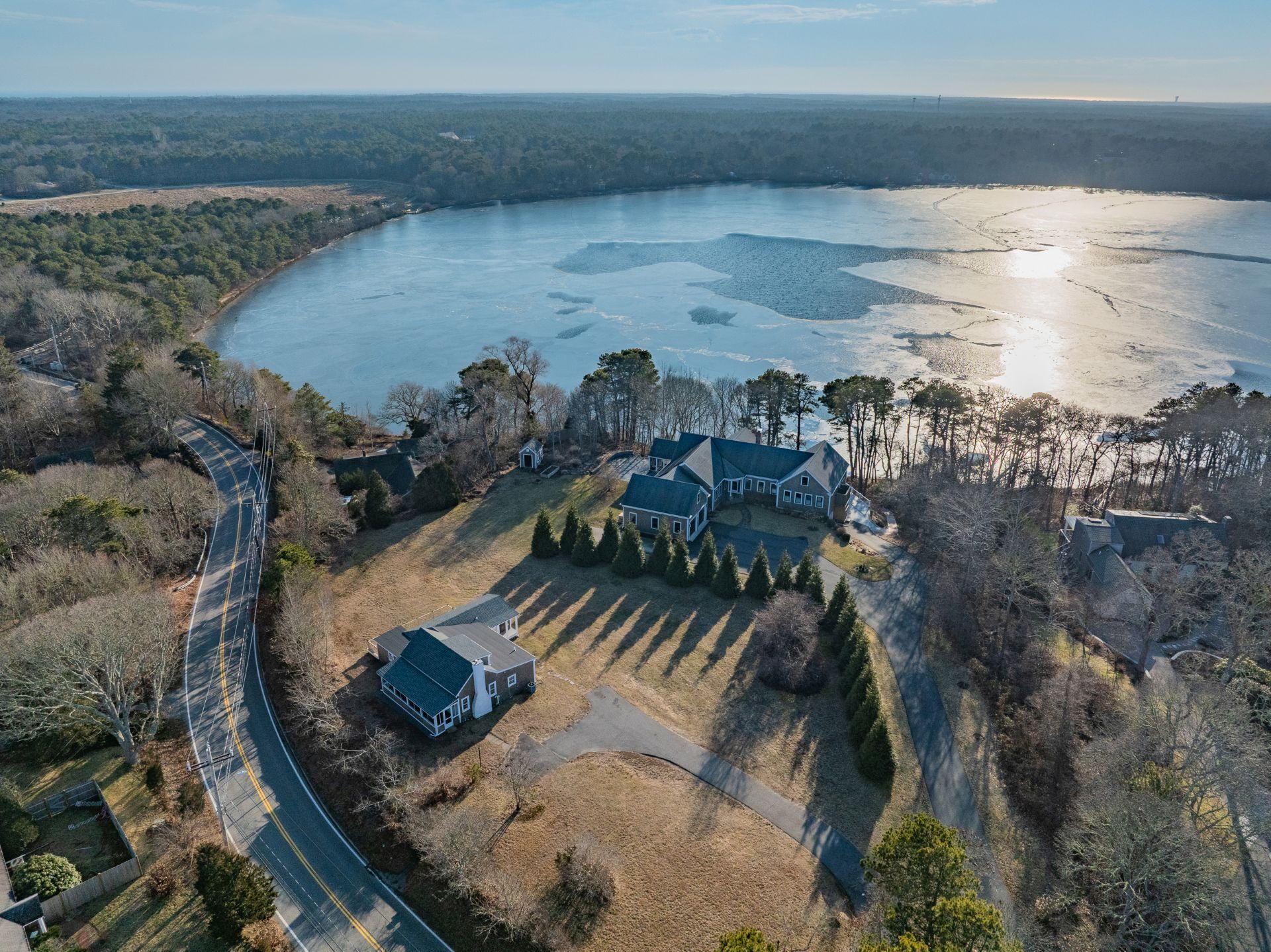 An aerial view of a lakeside property with a large house, a driveway, and a road curving around the property.