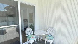 En patio med glasdør ind til et rum, to hvide metalstole med blomstrede hynder og et lille rundt bord.
