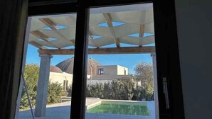 En vy genom ett fönster som visar ett poolområde med en pergola ovanför, en pool och en byggnad med en kupol i bakgrunden.