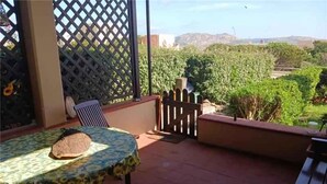 Eine Terrasse mit Tisch und Stuhl, ein Gitterzaun und Blick auf Grünflächen sowie entfernte Gebäude.
