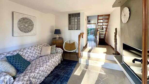Un salon moderne comprenant un canapé, un ventilateur, une chaise en bois, un téléviseur et un escalier menant à une autre pièce.
