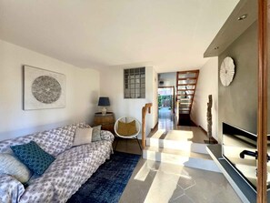 Ein modernes Wohnzimmer mit einer Couch, einem Ventilator, einem Holzstuhl, einem Fernseher und einer Treppe, die in einen anderen Raum führt.