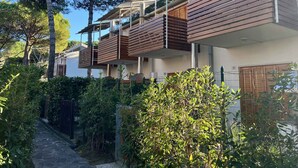 Un immeuble résidentiel moderne doté de nombreux balcons, entouré d’une végétation luxuriante et bordé d’un chemin en pierre.