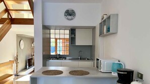 Une cuisine moderne avec un îlot central, une cuisinière encastrée et un four à micro-ondes. L’îlot est agrémenté de deux tabourets blancs et d’une machine à café.