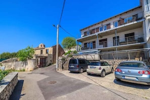 A street view with a two-story building, parked cars, and a clear blue sky. - Holiday flat with sea view and air conditioning (Crikvenica)