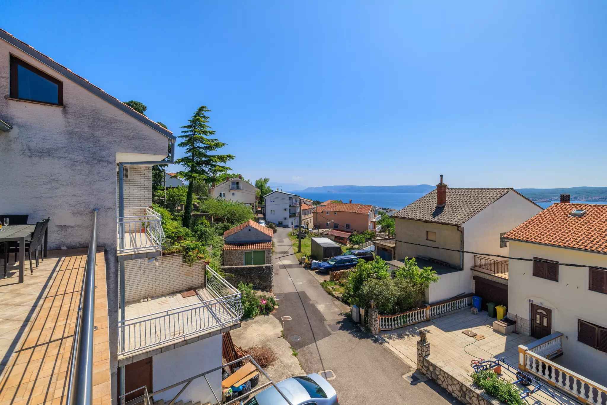 Una calle residencial con casas, cielo despejado y vista al mar.