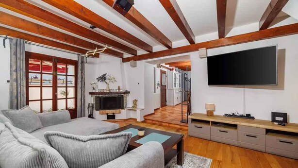 Una sala de estar con sofá, mesa de centro y televisión. Hay una chimenea, una planta y una puerta que da a otra habitación.
