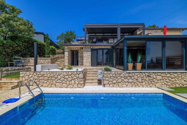 Ein modernes Haus mit Swimmingpool, Steinmauern und einem Balkon mit Gartenmöbeln.