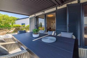 Eine Terrasse im Freien mit einem dunklen Tisch, Korbstühlen und einem Blumentopf.