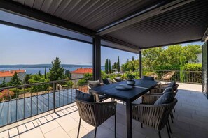Ein Balkon mit Tisch und Stühlen im Freien, mit Blick auf ein Gewässer und Grünflächen.