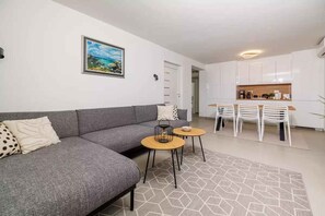 A modern living room with a grey sofa, a dining area with white chairs, and a kitchen in the background. - Holiday home with private pool and sea view (Selce)