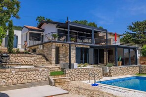 Ein modernes Haus mit Natursteinfassade, einem Swimmingpool und einer überdachten Terrasse mit Sitzgelegenheiten.
