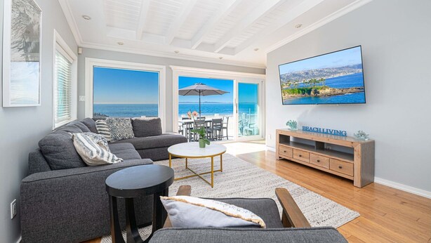 Amplia sala de estar con un televisor grande, sofá gris y vista al mar a través de ventanas amplias.