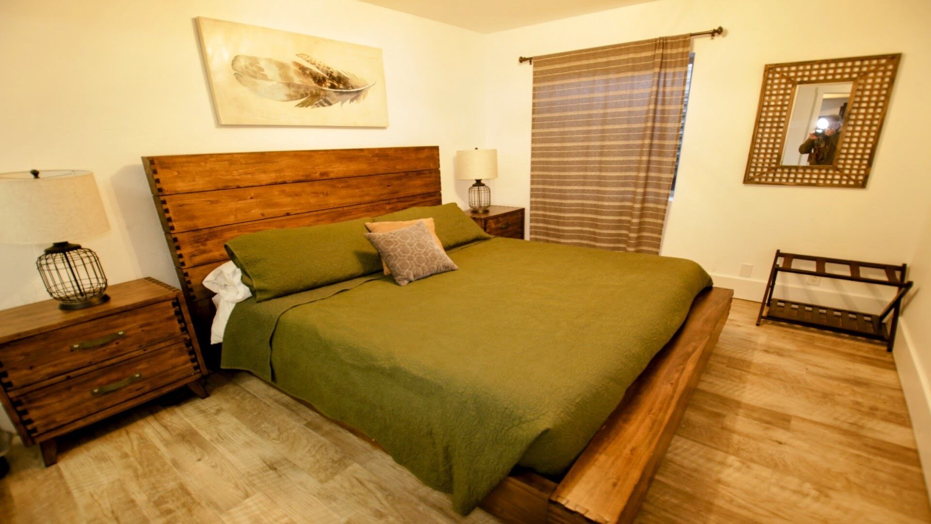 Ein ordentlich eingerichtetes Schlafzimmer mit einem hölzernen Bett, einem Nachttisch mit Lampe, einer kleinen Holzschatulle und einem Spiegel an der Wand.