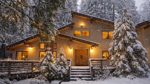 Eine Holzhütte mit beleuchtetem Eingang, umgeben von schneebedeckten Bäumen.