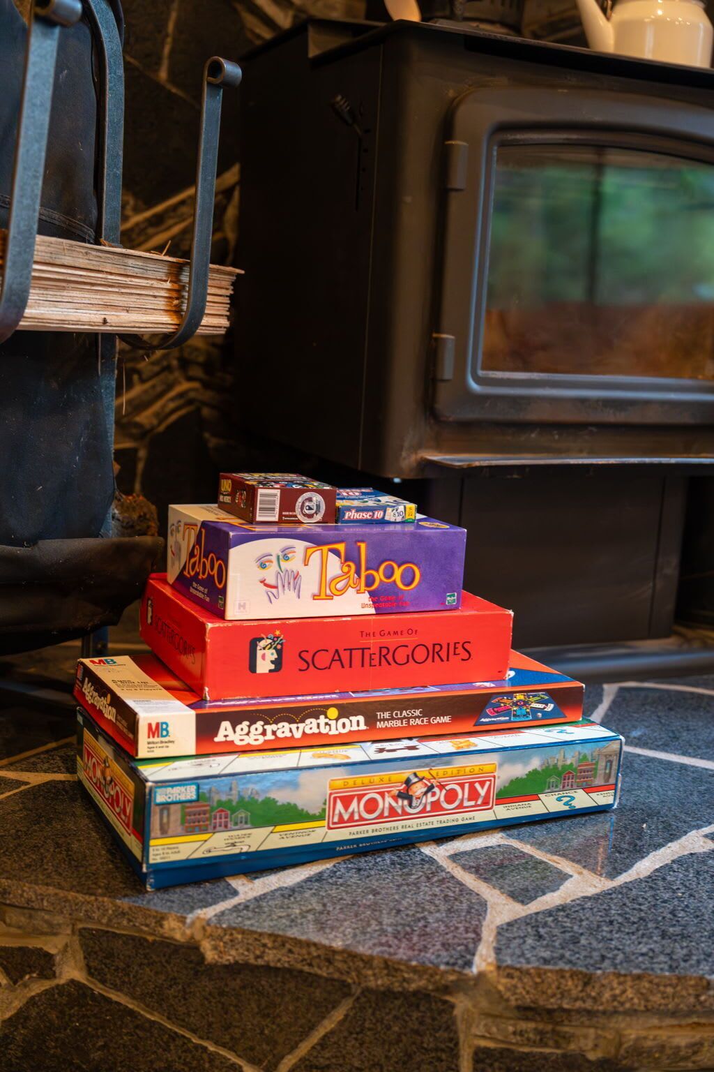 Une pile de jeux de société, dont Taboo, Scattergories, Aggravation et Monopoly, est posée sur un sol en pierre.