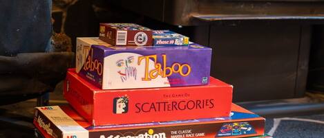 Une pile de jeux de société, dont Taboo, Scattergories, Aggravation et Monopoly, est posée sur un sol en pierre.