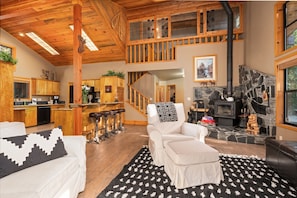 A spacious living area with a fireplace, wooden ceiling, and a kitchen with wooden cabinets. - Peaceful Cabin Getaway, Relaxing By the Creek, Walking Distance to Town (Shaver Lake)